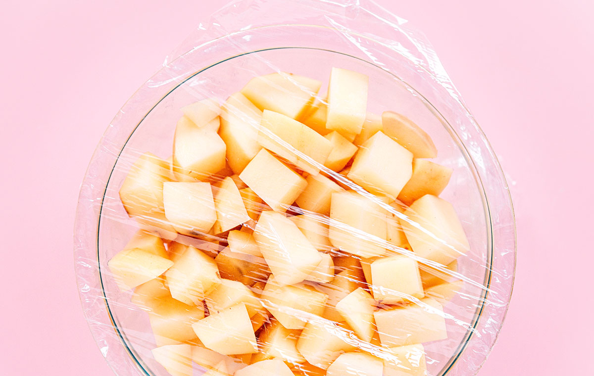 diced and peeled white potatoes in a glass bowl with plastic wrap covering them.