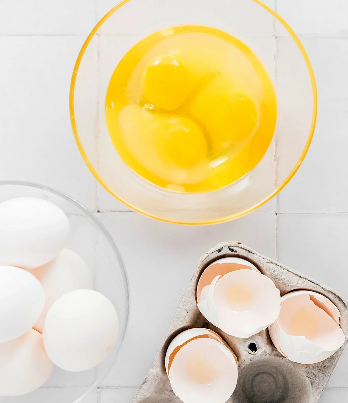 Egg yolks and whites in a bowl next to shells
