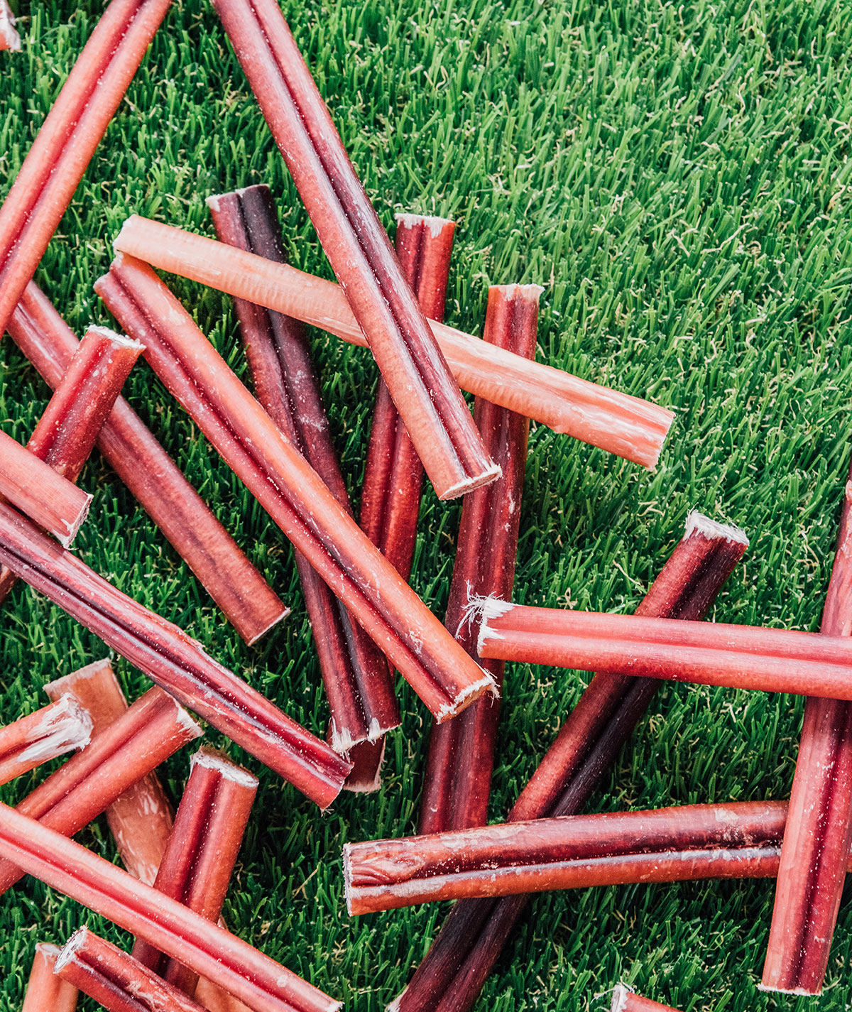 Bully sticks spread out on grass with some overlapped on each other.