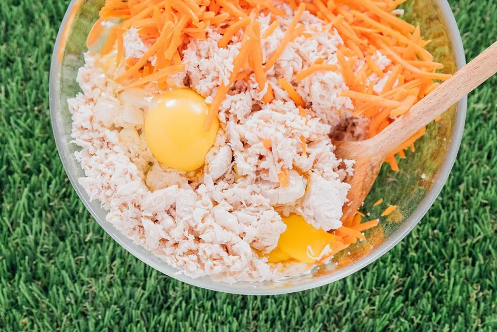 Shredded chicken, eggs, carrots, and flour in a bowl with a wooden spoon.