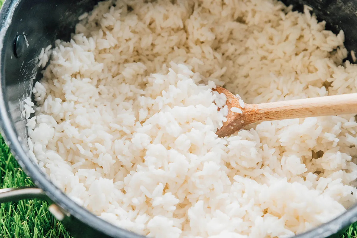 A pot of cooked white rice with  wooden spoon.