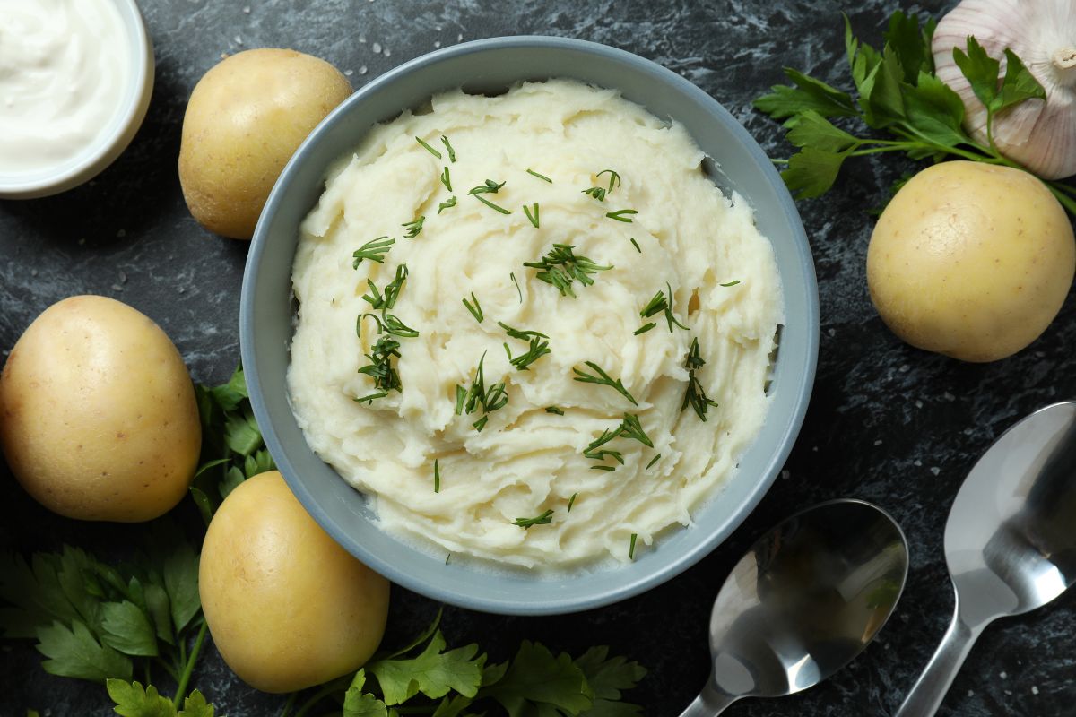 Mashed potatoes in a bowl surrounded by yellow potatoes.