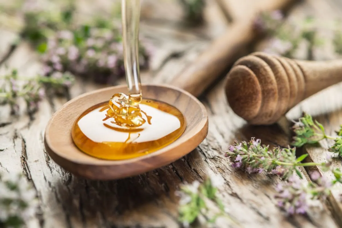 Honey being poured into a spoon next to herbs.