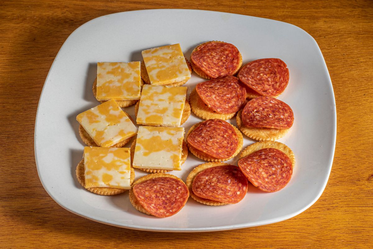 Ritz crackers with cheese and sausage on them on a white plate.