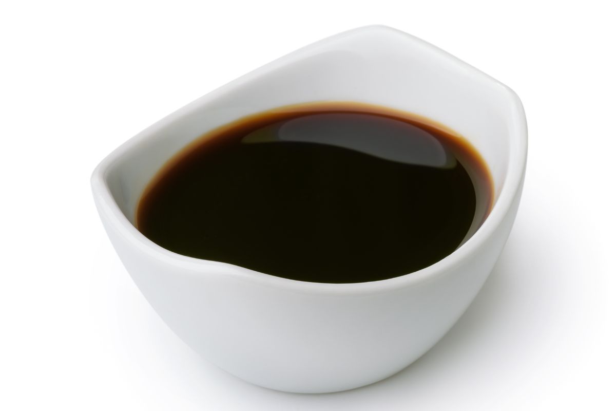 A white bowl of soy sauce on a white background.